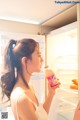 A woman standing in front of an open refrigerator holding a bottle of juice.