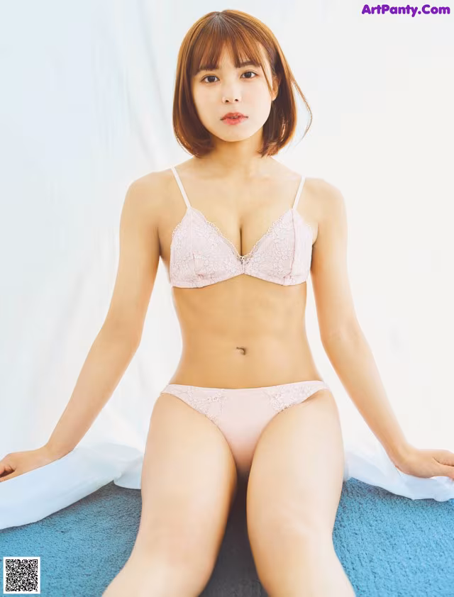 A woman in a pink bra and panties sitting on a blue rug.