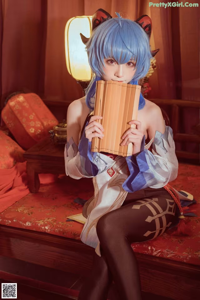 A woman with blue hair sitting on a red couch holding a pan flute.