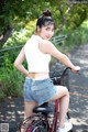 A woman in a white top and denim shorts riding a bike.