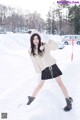 A woman in a white sweater and black skirt posing in the snow.