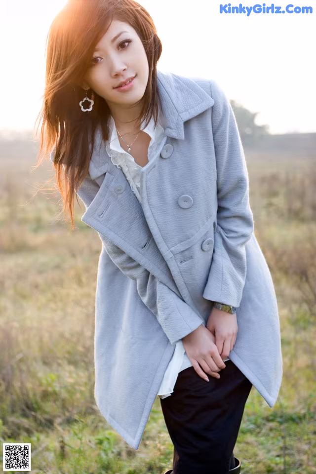 A woman in a gray coat standing in a field.