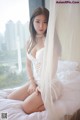 A woman sitting on a bed in a white lingerie.