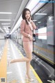 A woman in a pink suit is standing on a subway platform.