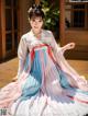 A woman in a pink and blue hanbok sitting on a wooden floor.