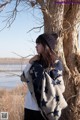 A woman leaning against a tree with a blanket around her neck.