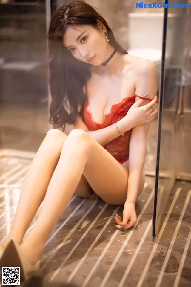 A woman in a red lingerie sitting on the floor.