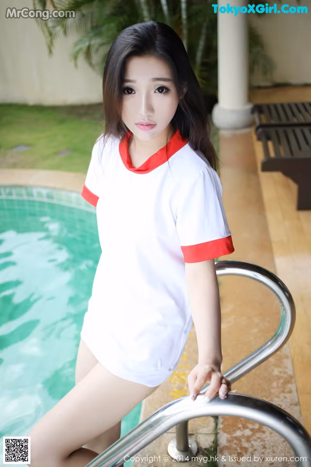 A woman in a white and red shirt leaning on a railing by a pool.