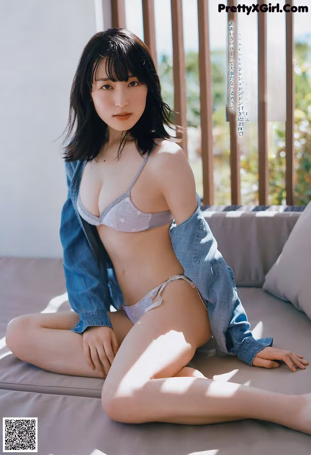 A woman sitting on top of a bed wearing a blue shirt.