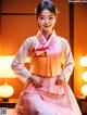 A woman in a pink and orange hanbok poses for a picture.