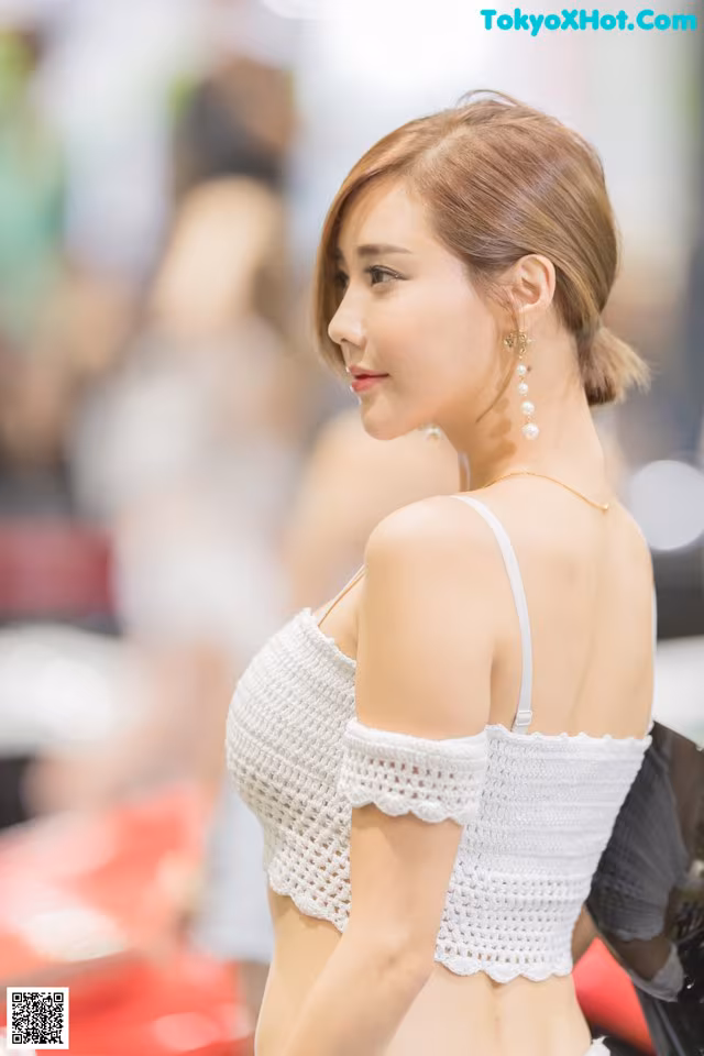 A woman in a white top and skirt standing next to a car.