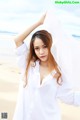 A woman in a white shirt is posing on the beach.