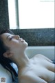 A naked woman laying in a bathtub with water droplets on her body.